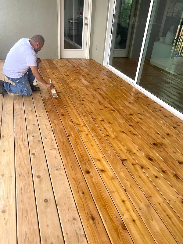 Deck stain being applied to wood boards near the sliding glass door