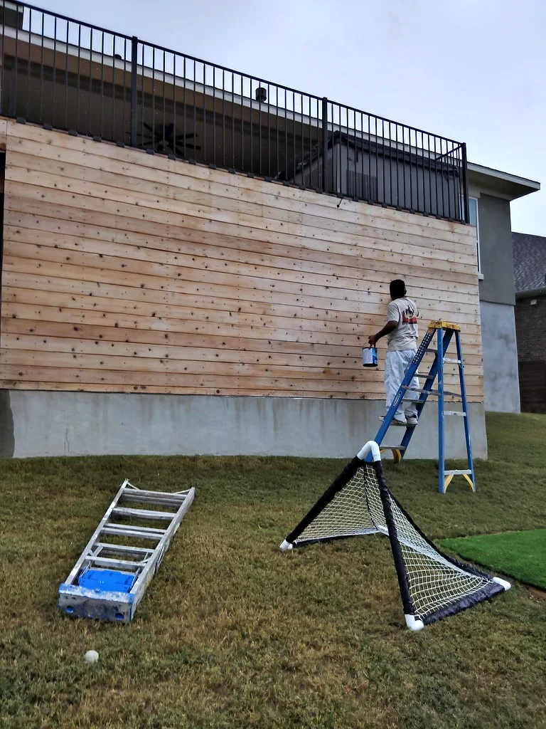 Painter staining the exterior wood storage unit below a Bee Cave deck