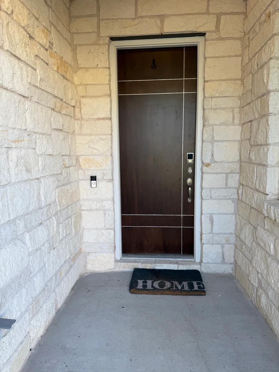 Finished Bee Cave front door with dark finish, hardware, light trim, limestone entry, and welcome mat