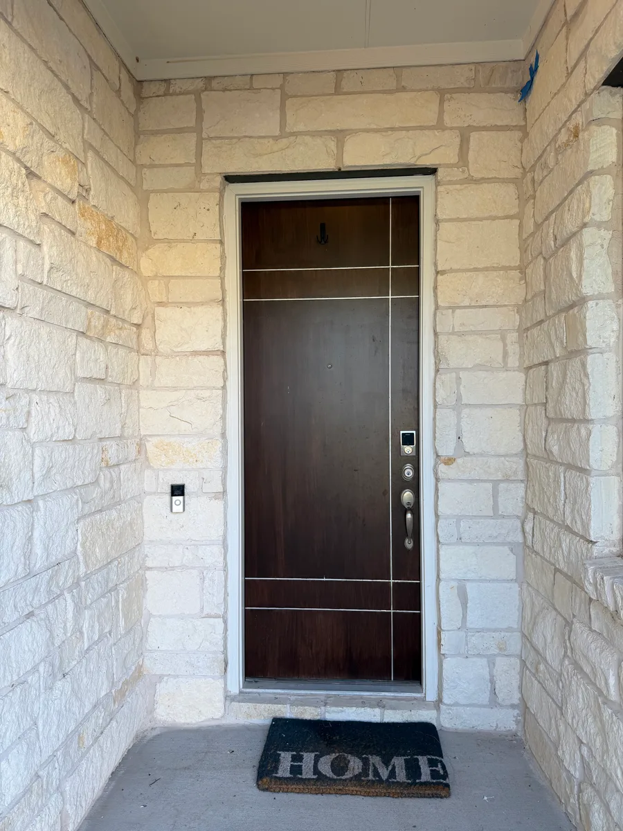 Bee Cave front door finished view with covered porch, limestone walls, trim, and dark door finish