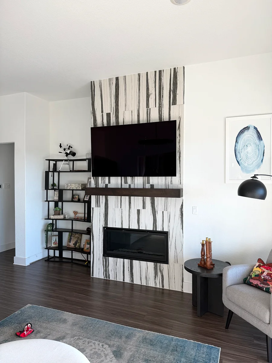 Finished Bee Cave living room with white interior walls, wall tile feature, fireplace, TV, and open shelving