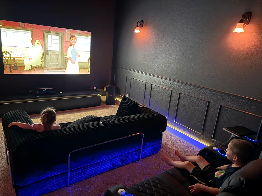 Finished Dripping Springs media room with dark paint, wall panel trim, seating, screen, sconces, and accent lighting