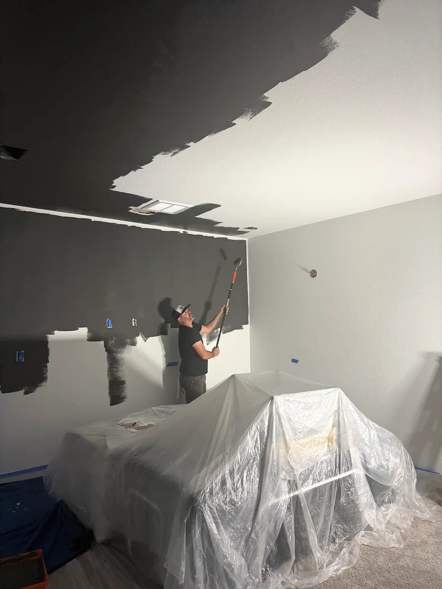Painter rolling dark paint in a protected Dripping Springs media room
