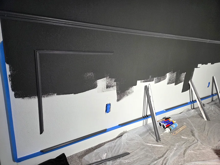 Media room wall panel trim and dark paint in progress with plastic floor protection