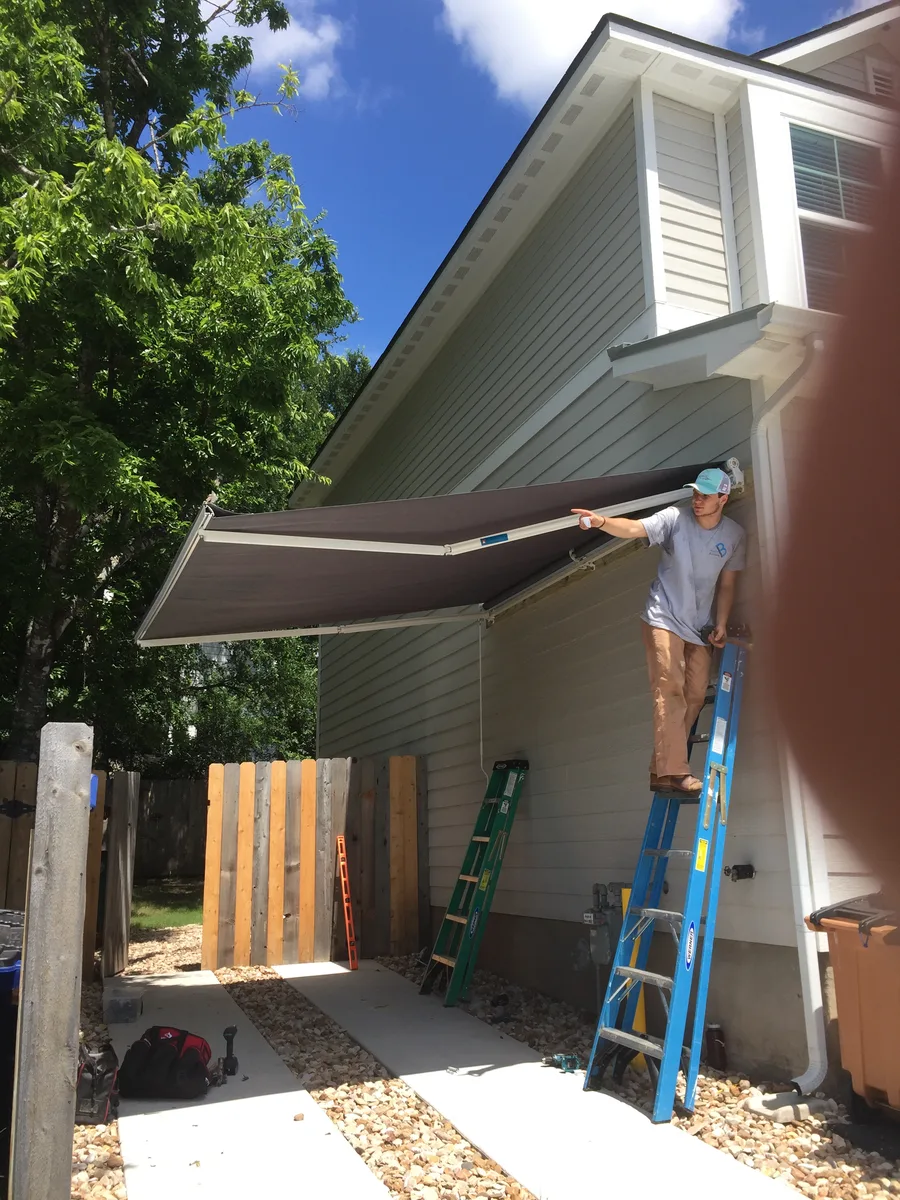 East Austin exterior awning installation in progress with ladder access beside the house siding