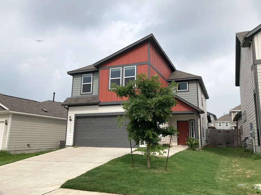 Finished Pflugerville house exterior with painted siding, garage door, trim, and red accent siding